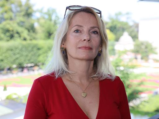 Joanna Bator steht im roten Kleid im Freien in einem Park