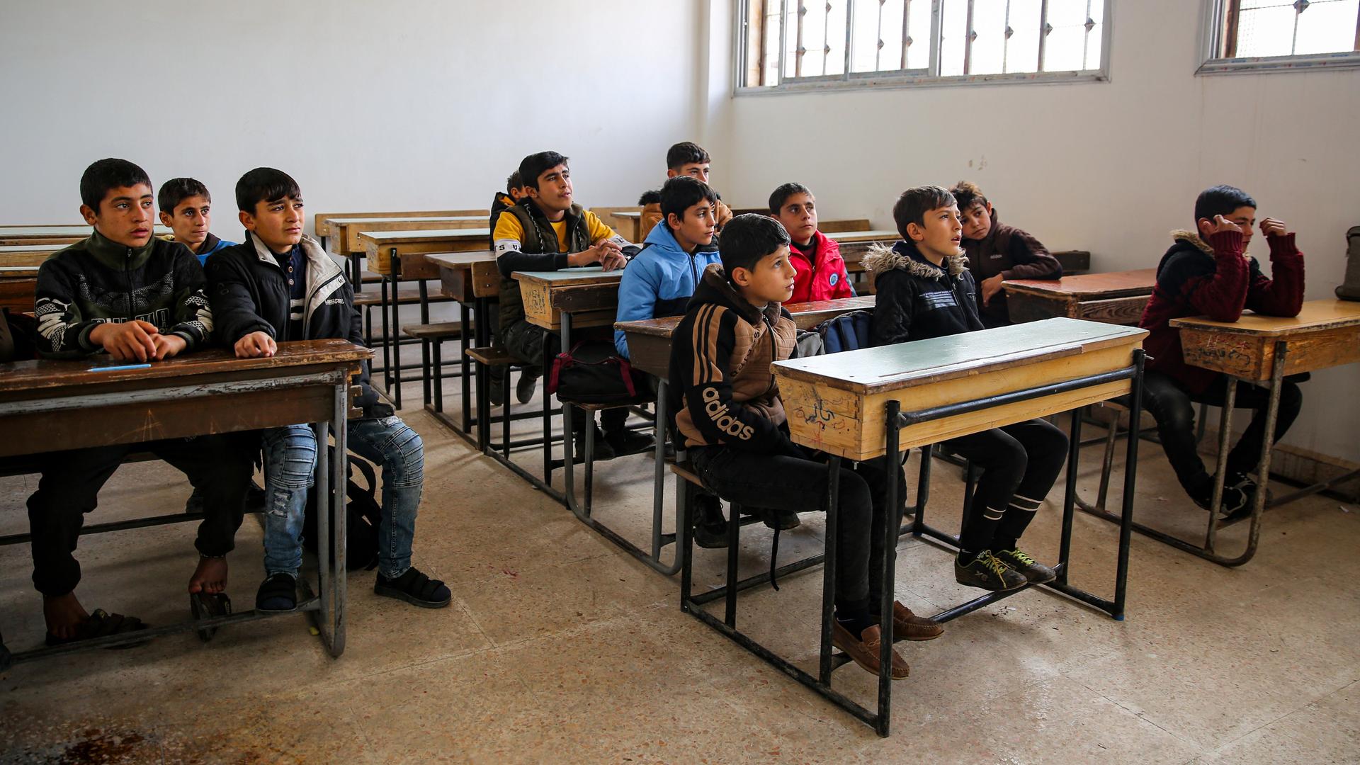 12 Jungen sitzen in einem Schulraum. Die Schule ist in der Stadt Aleppo in Syrien. 