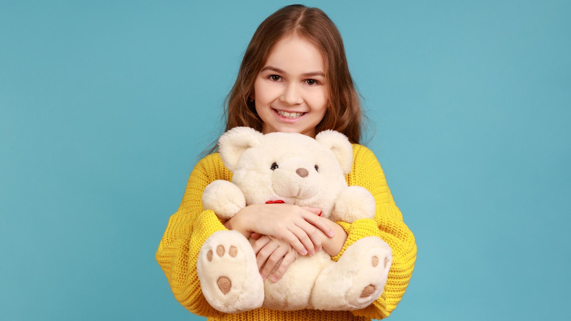 Ein Mädchen mit langen Haaren und im gelben Pullover umarmt einen Teddybär Ein Mädchen mit langen Haaren und im gelben Pullover umarmt einen Teddybär