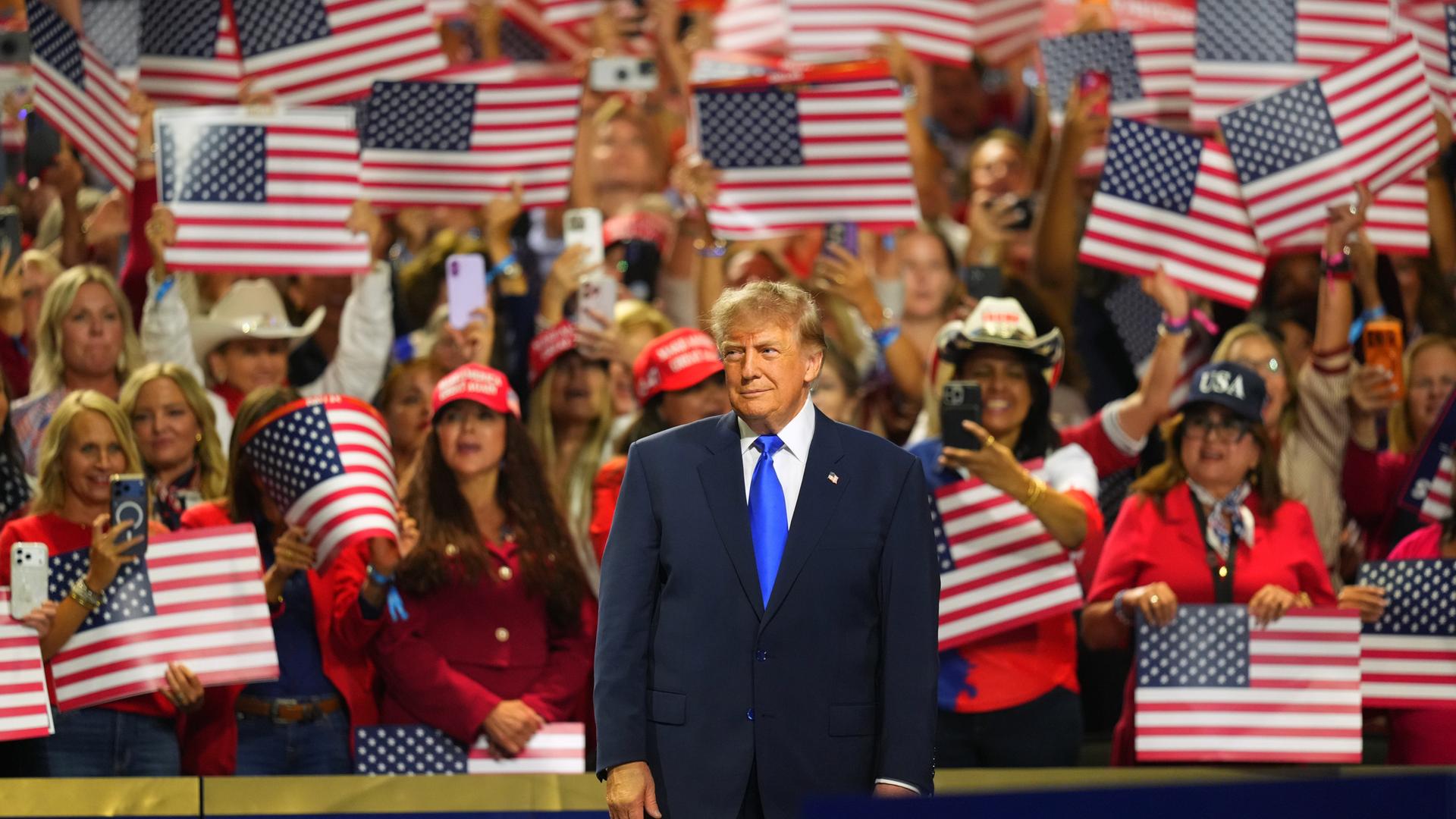US-Präsident Trump beim Parteitag der Republikaner in Dallas. Er steht auf einer Bühne. Hinter ihm jubeln Anhänger mit US-Flaggen.