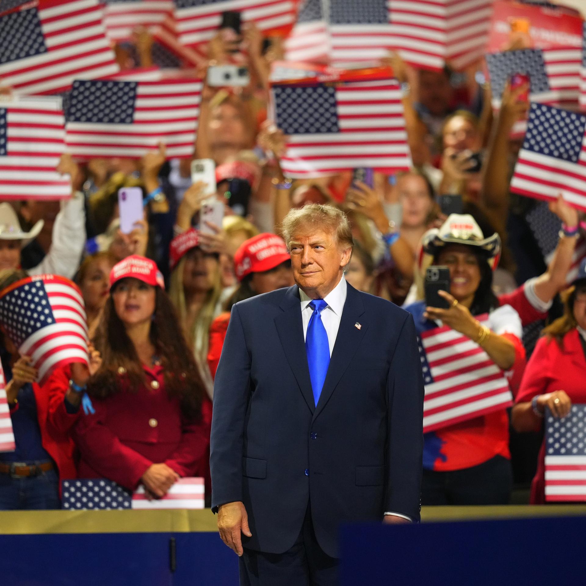 US-Präsident Trump beim Parteitag der Republikaner in Dallas. Er steht auf einer Bühne. Hinter ihm jubeln Anhänger mit US-Flaggen.
