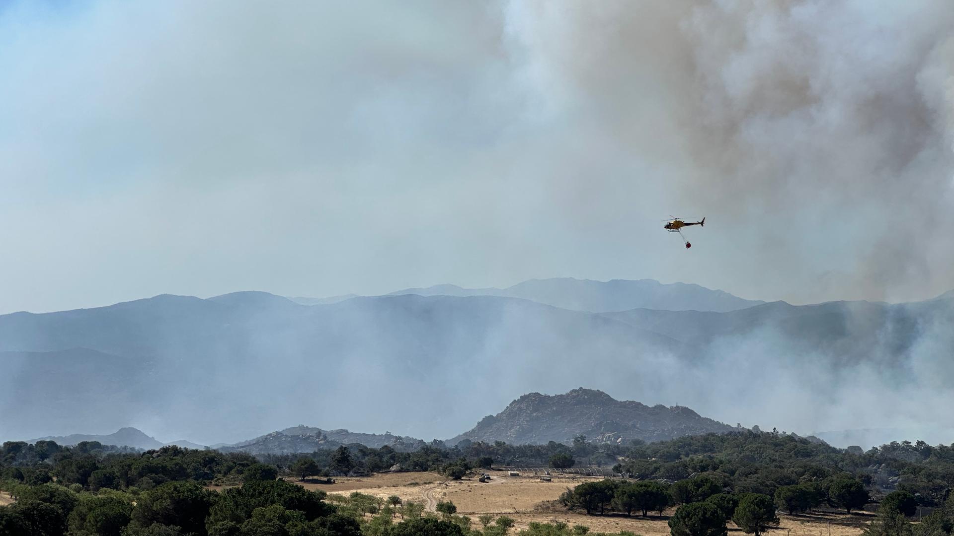 Feuerwehrleute bekämpfen einen Großbrand in der Nähe von Montalba-le-Château - ein Löschhubschrauber überfliegt das Gebiet. 