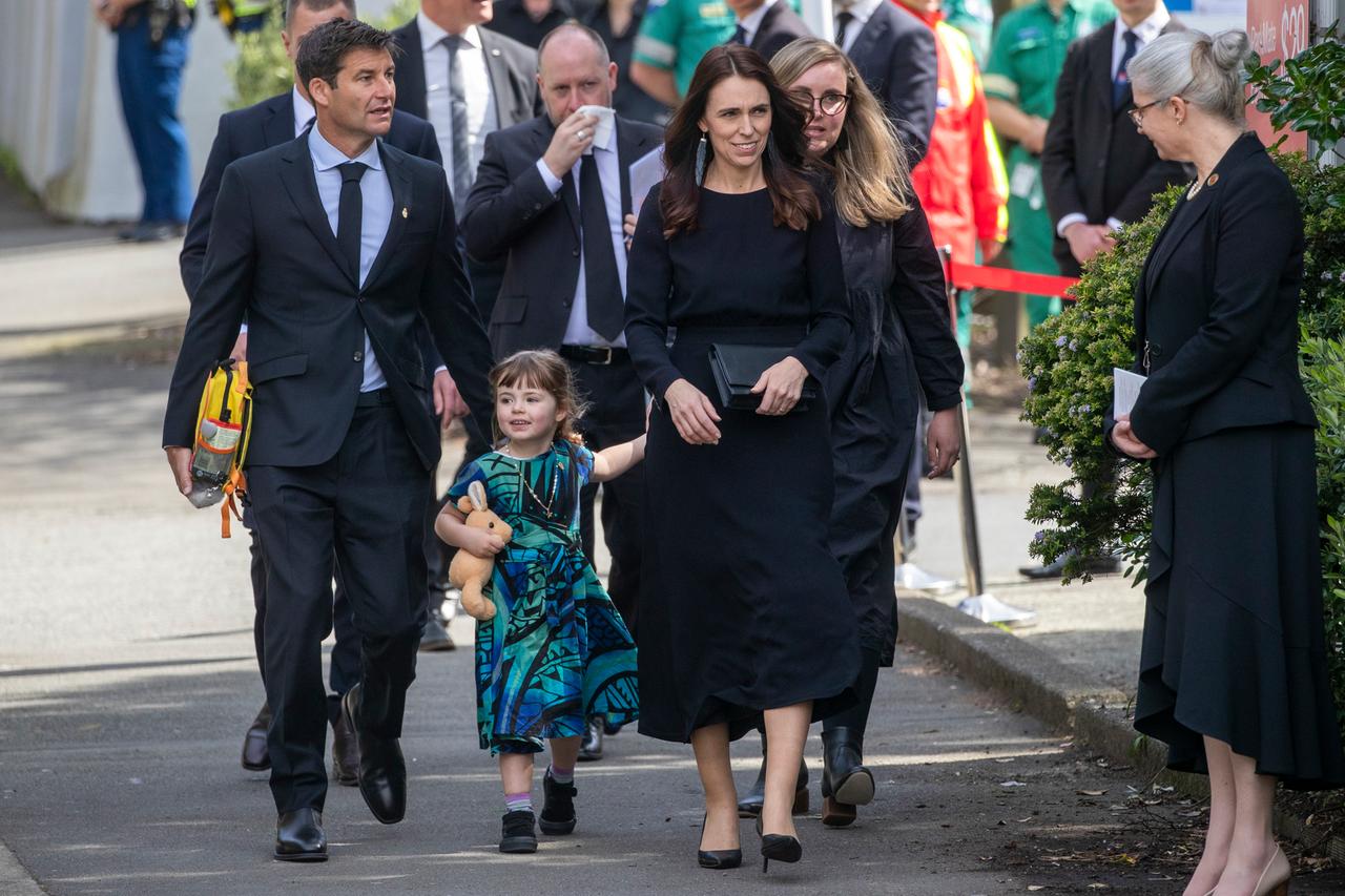 Eine Personengruppe geht auf einer Straße entlang. Eine schwarzgekleidete Frau geht voran, sie hält ein kleines Mädchen in einem blaugrün-schwarzgemusterten Kleid an der Hand. Es ist Neuseelands Premierministerin Jacinda Ardern mit ihrer Familie.