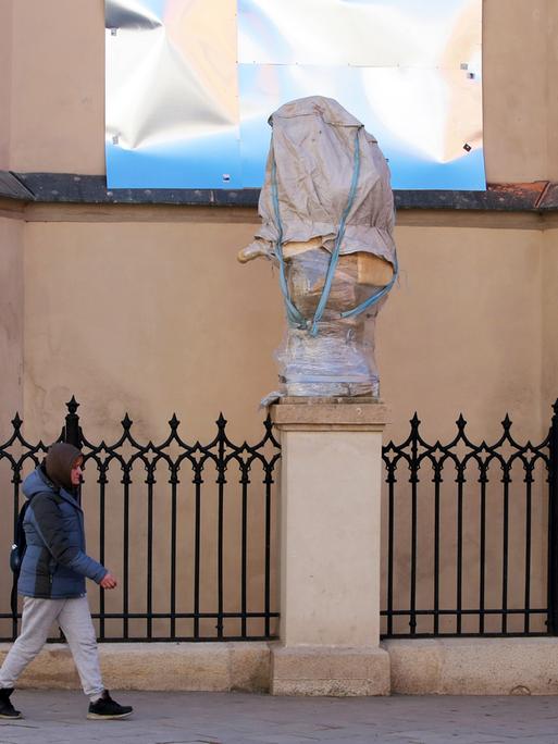 Eine Passantin geht an einer verhüllten und verpackten Statue vorbei.