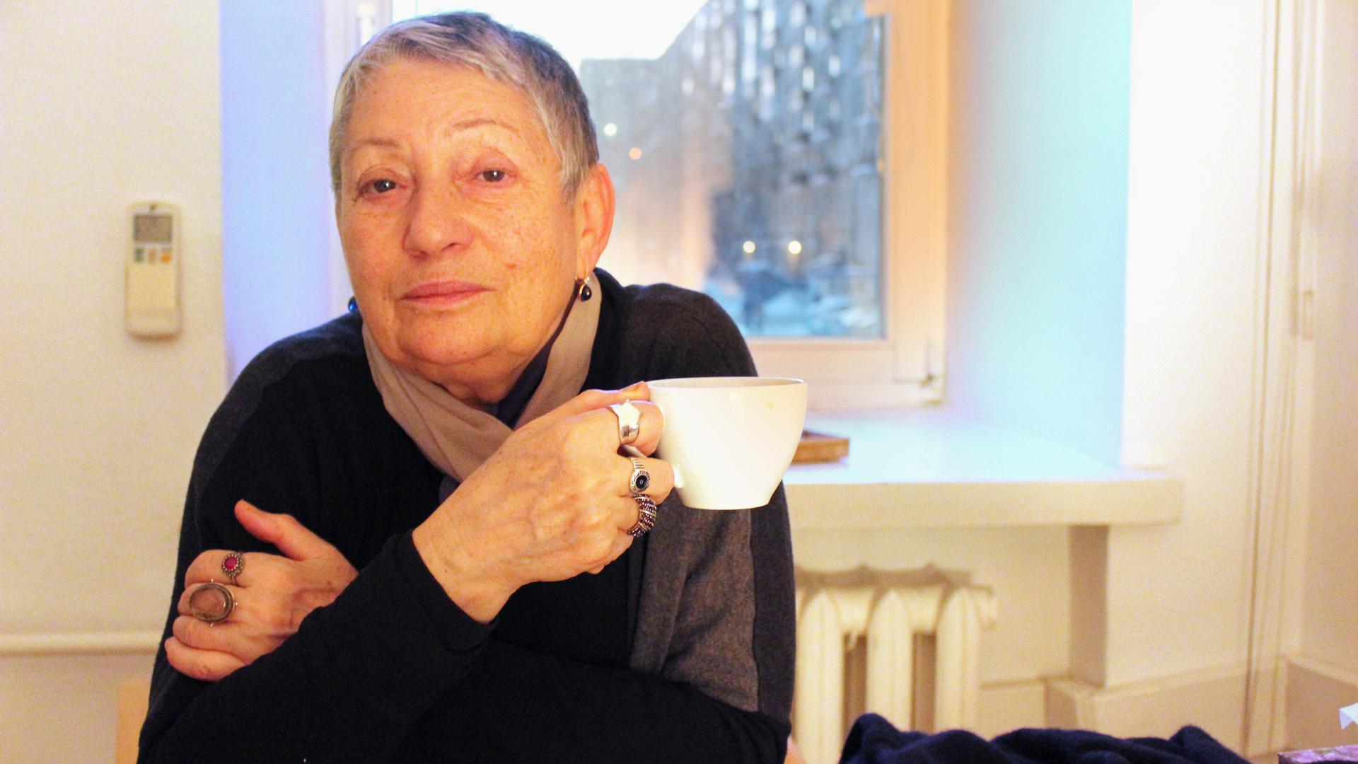 Die russische Schriftstellerin Ljudmila Ulitzkaja hält eine Tasse in der Hand und blickt in die Kamera. 