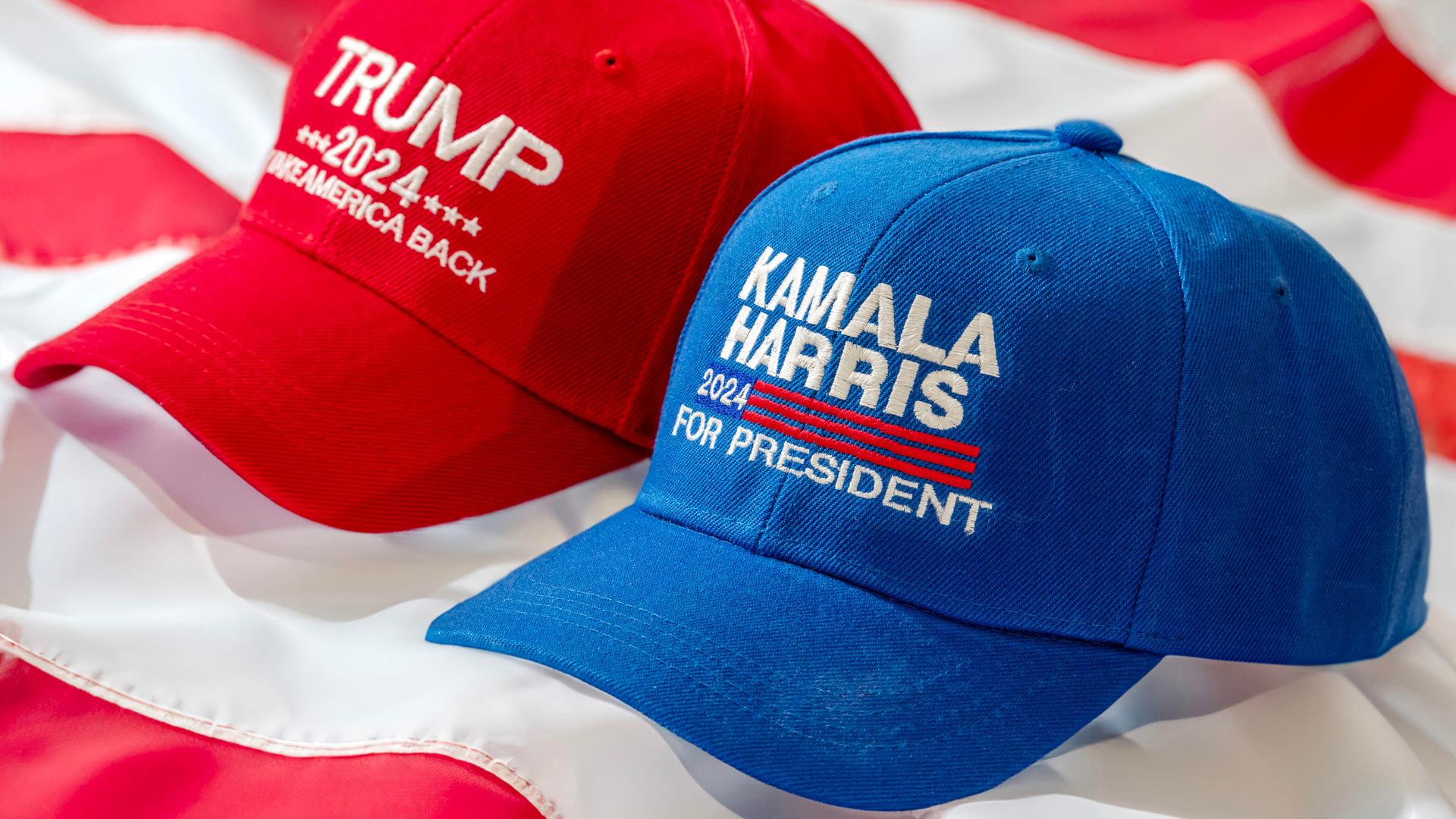 Rote Trump Basecap und blaue Kamala Harris Kappe liegen nebeneinander. 