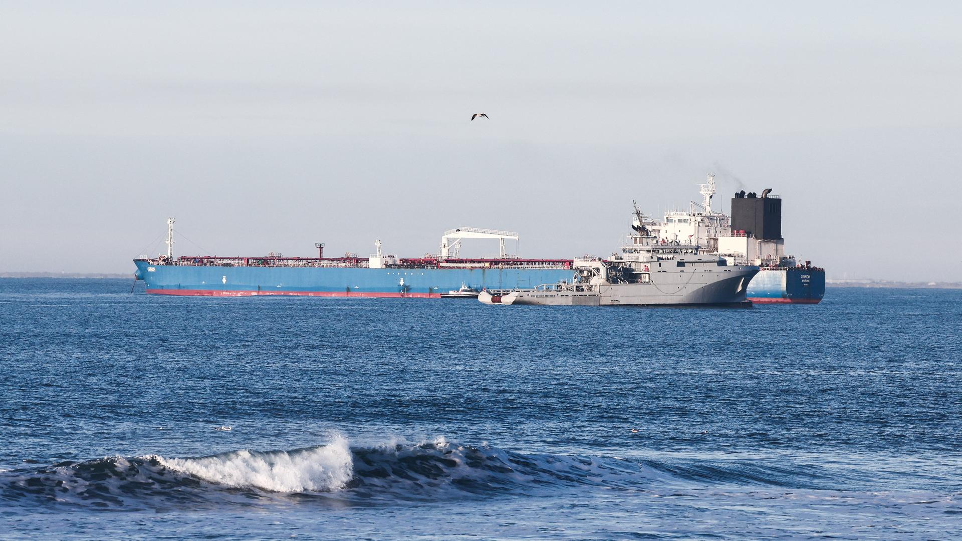 Blick auf einen Öltanker mit blauem Rumpf. Davor kreuzt ein französisches Kriegsschiff Blick auf einen Öltanker mit blauem Rumpf. Davor kreuzt ein französisches Kriegsschiff