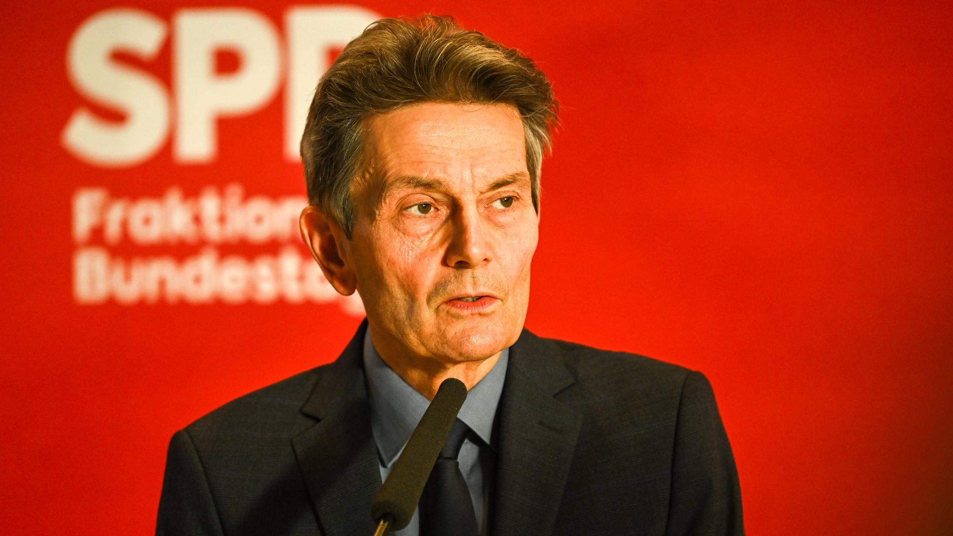 Der SPD-Fraktionsvorsitzende Rolf Mützenich steht vor einer roten Wand mit SPD-Logo.
