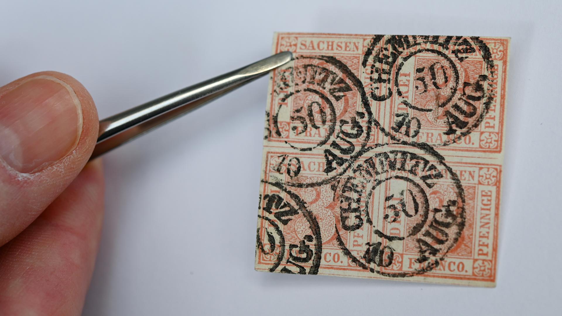 Eine Hand hält mit einer Pinzette den Viererblock einer roten Briefmarke: Die Marke ist als "Sachsendreier" bekannt.