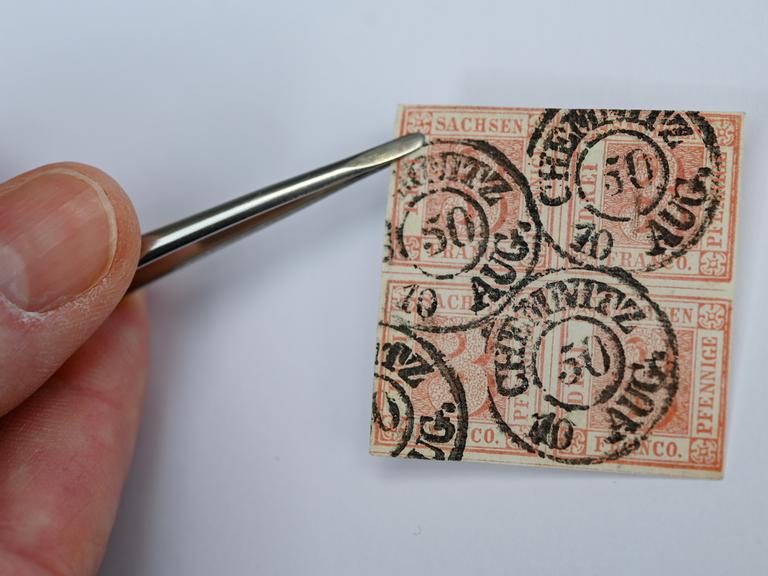 Eine Hand hält mit einer Pinzette den Viererblock einer roten Briefmarke: Die Marke ist als "Sachsendreier" bekannt.