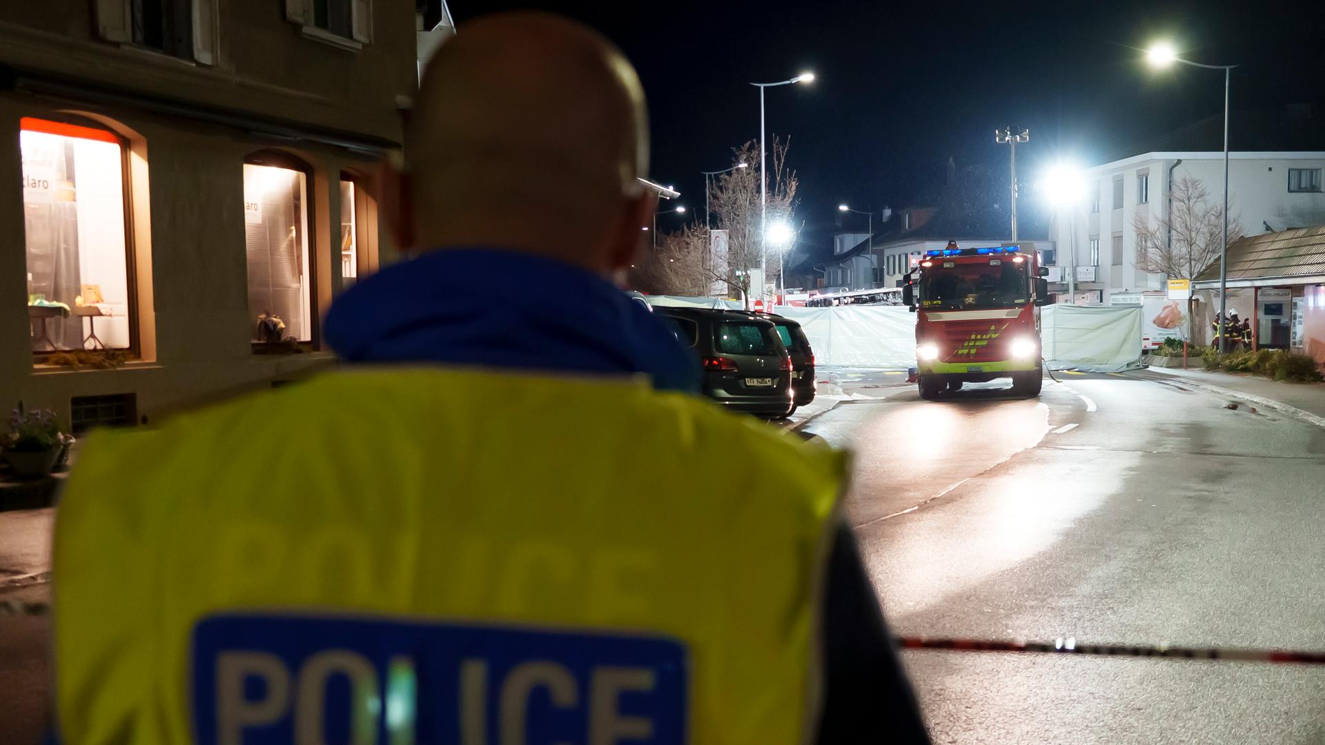 Eine nächtliche Straße; ein Polizist mit Warnweste steht vor einem Feuerwehrauto.