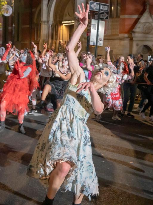 Menschen in verschiedenen Halloween-Kostümen tanzen mit merkwürdig verrenkten Gliedmaßen.