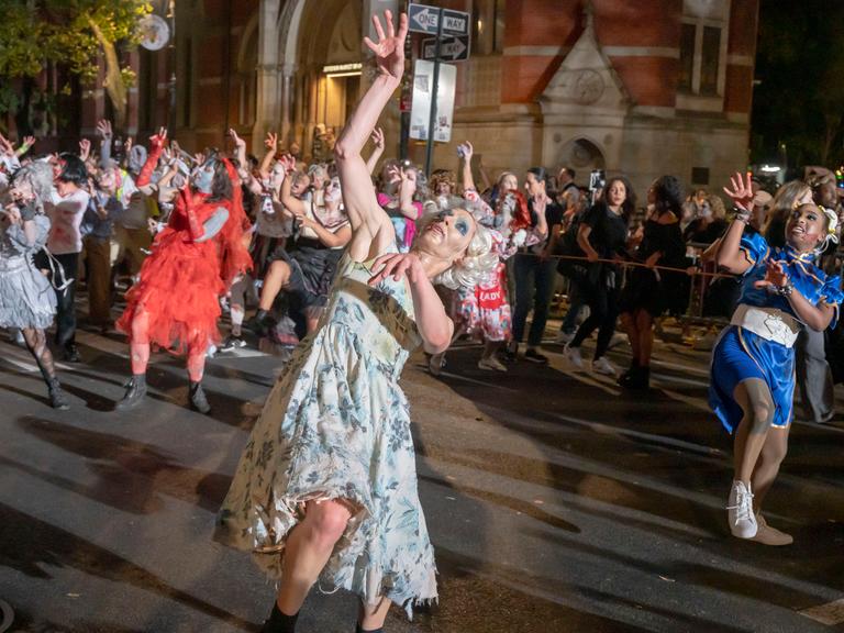 Menschen in verschiedenen Halloween-Kostümen tanzen mit merkwürdig verrenkten Gliedmaßen.