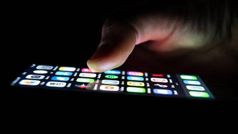 Ein Mann hält ein iPhone in seiner Hand, auf dem Application Apps zu sehen sind. 