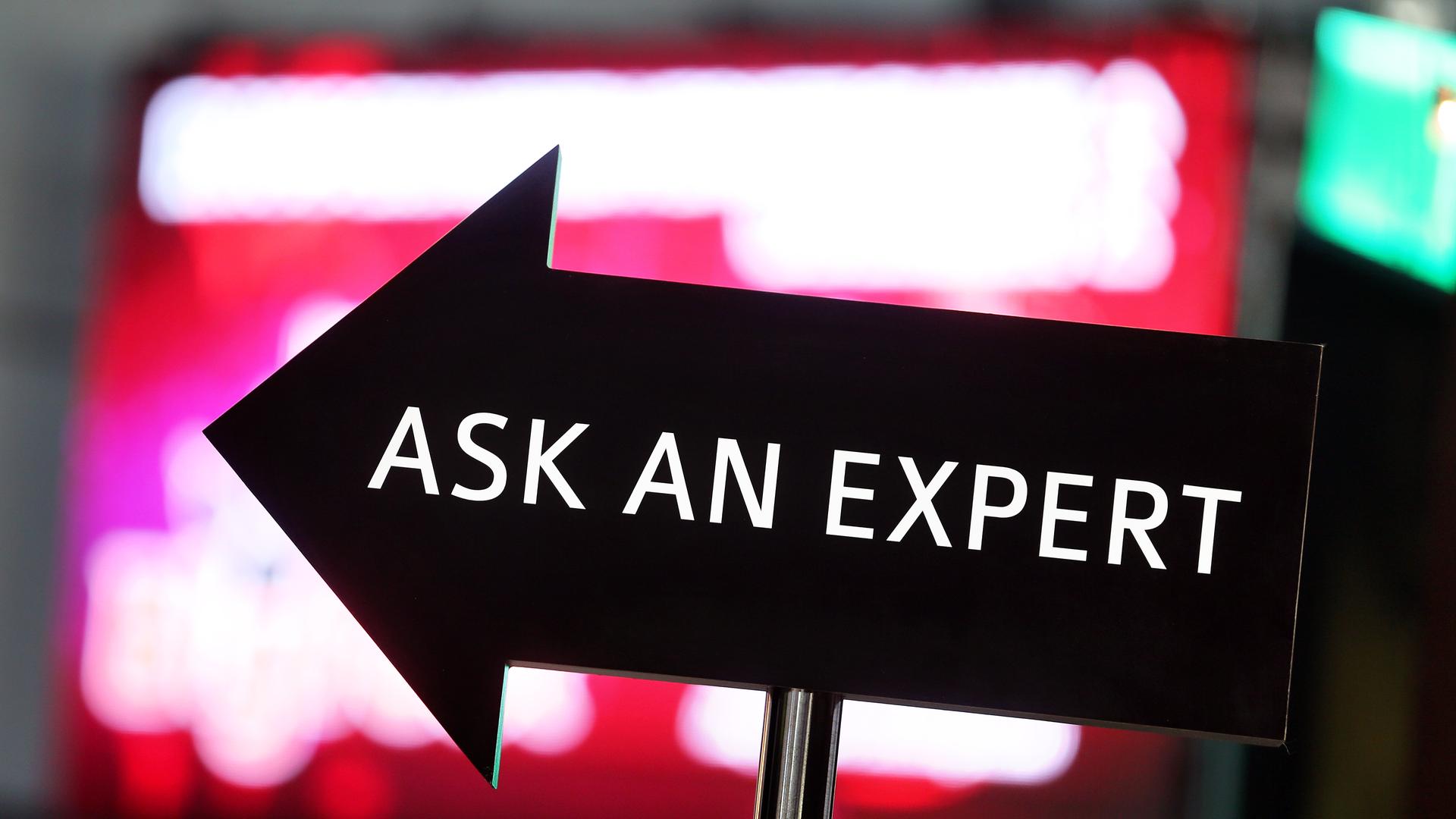 Ein Pfeil-Schild, auf dem "Ask an Expert" steht, vor dem Hintergrund eines roten Computerbildschirms