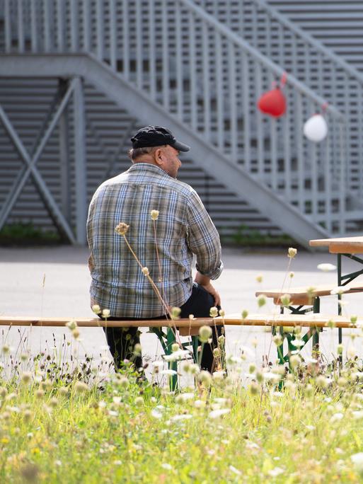 Ein Mann sitzt in Rückenansicht vor einer Flüchtlingsunterkunft in Bochum. 