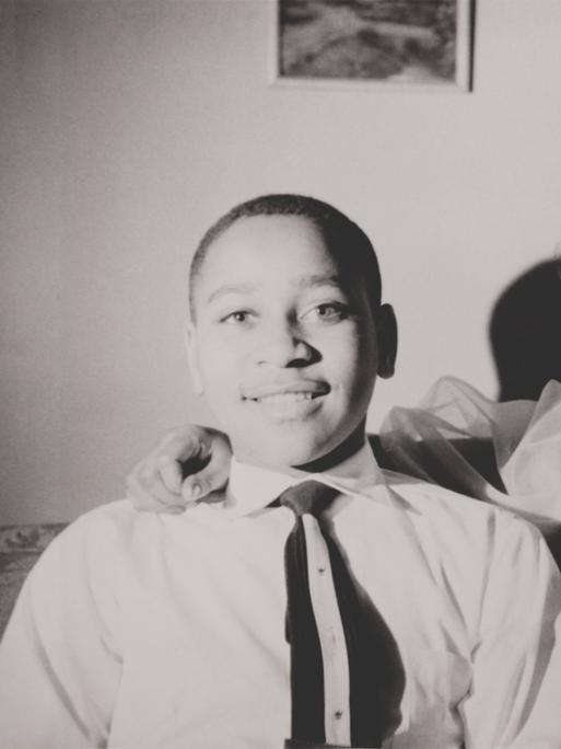 Schwarzweiß-Familienschnappschuss: Emmett Till sitzt fröhlich neben seiner Mutter Mamie Bradley, die freundlich lacht.