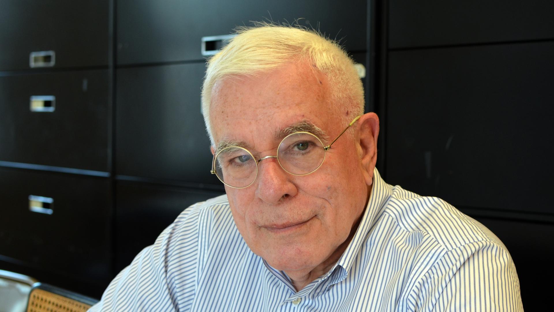 Der Architekt Peter Eisenman trägt ein gestreiftes Hemd und sitzt in seinem Büro vor einem schwarzen Schrank