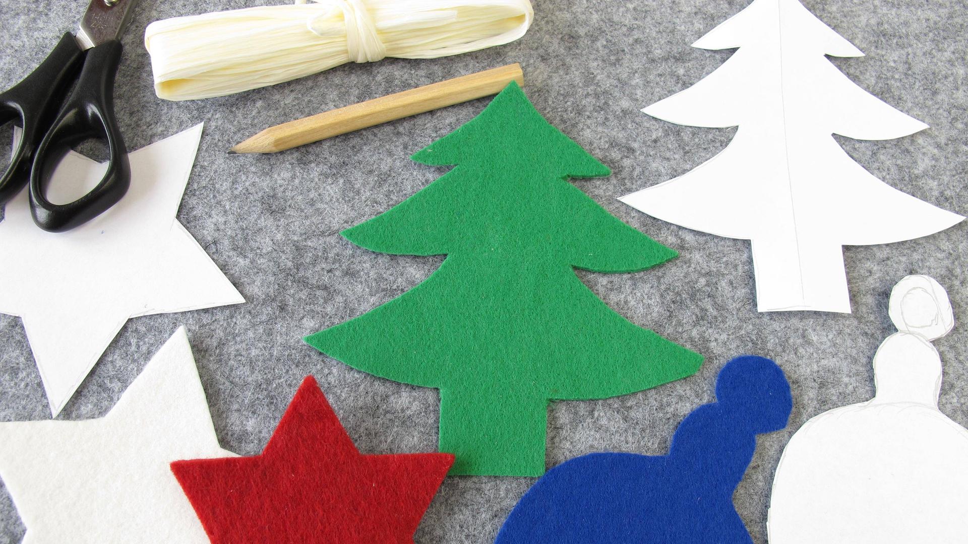 Eine Schere, ein Bleistift und verschiedene Motive auf Filz, darunter Sterne und ein Weihnachtsbaum, liegen auf einem Tisch. Eine Schere, ein Bleistift und verschiedene Motive auf Filz, darunter Sterne und ein Weihnachtsbaum, liegen auf einem Tisch.