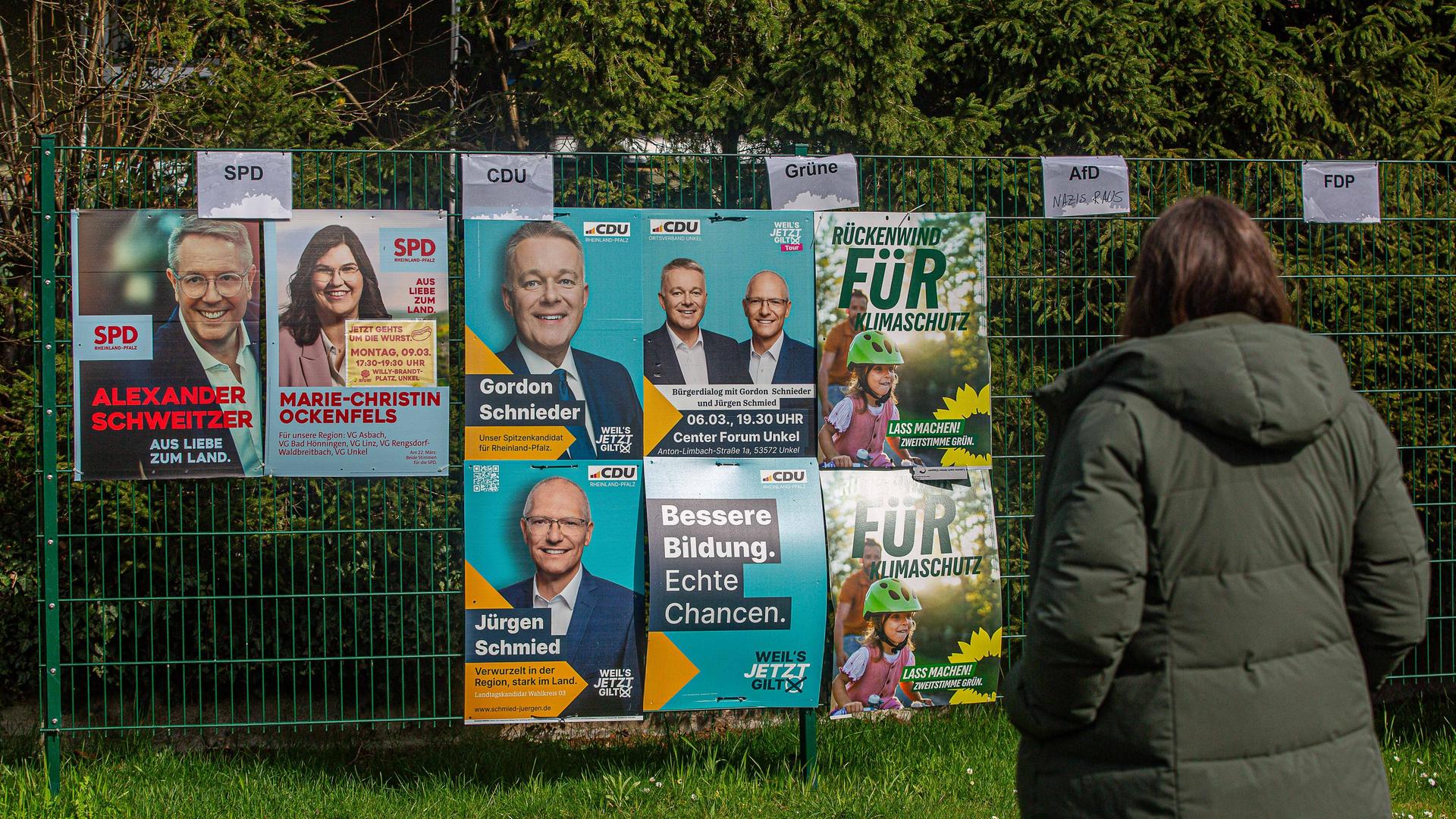 Eine Frau schaut auf Wahlplakate zur Landtagswahl in Rheinland-Pfalz, die an einem Zaun angebracht sind