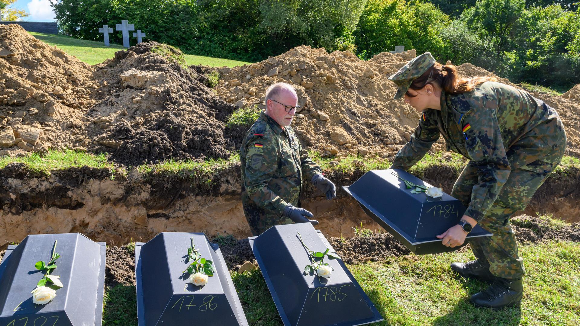 Das Bild zeigt zwei Bundeswehrsoldaten, die kleine Särge mit Gefallenen des Zweiten Weltkriegs auf der Kriegsgräberstätte Lietzen einbetten. 