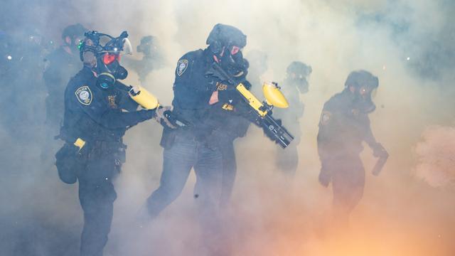 Bei einem Einsatz in Portland, Oregon im Februar 2026 stehen ICE-Agenten in Uniform und mit Masken in einer Wolke aus Tränengas und halten Tränengaswaffen in der Hand.