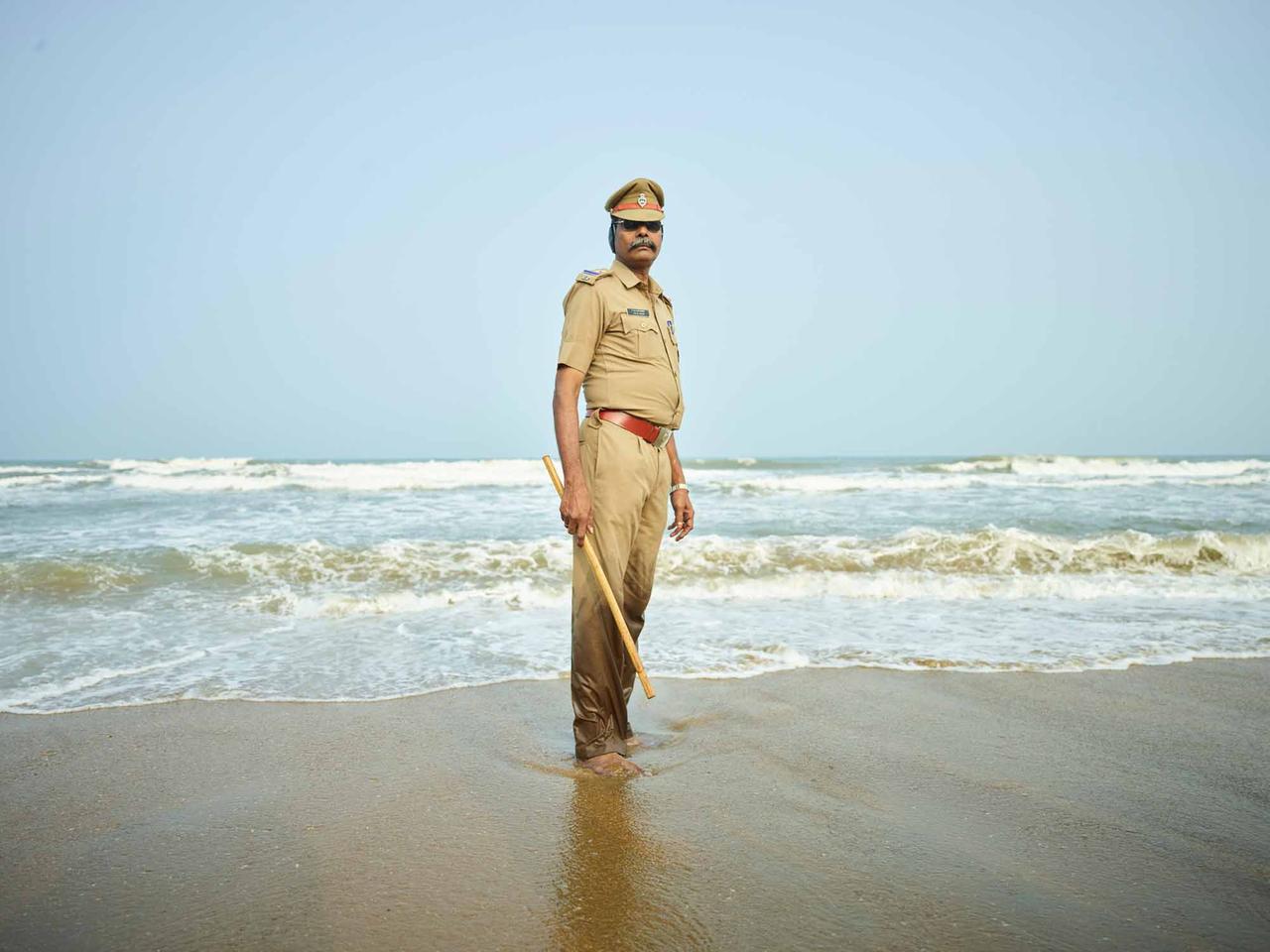 Ein indischer Polizist am Strand, mit Stock in der Hand.