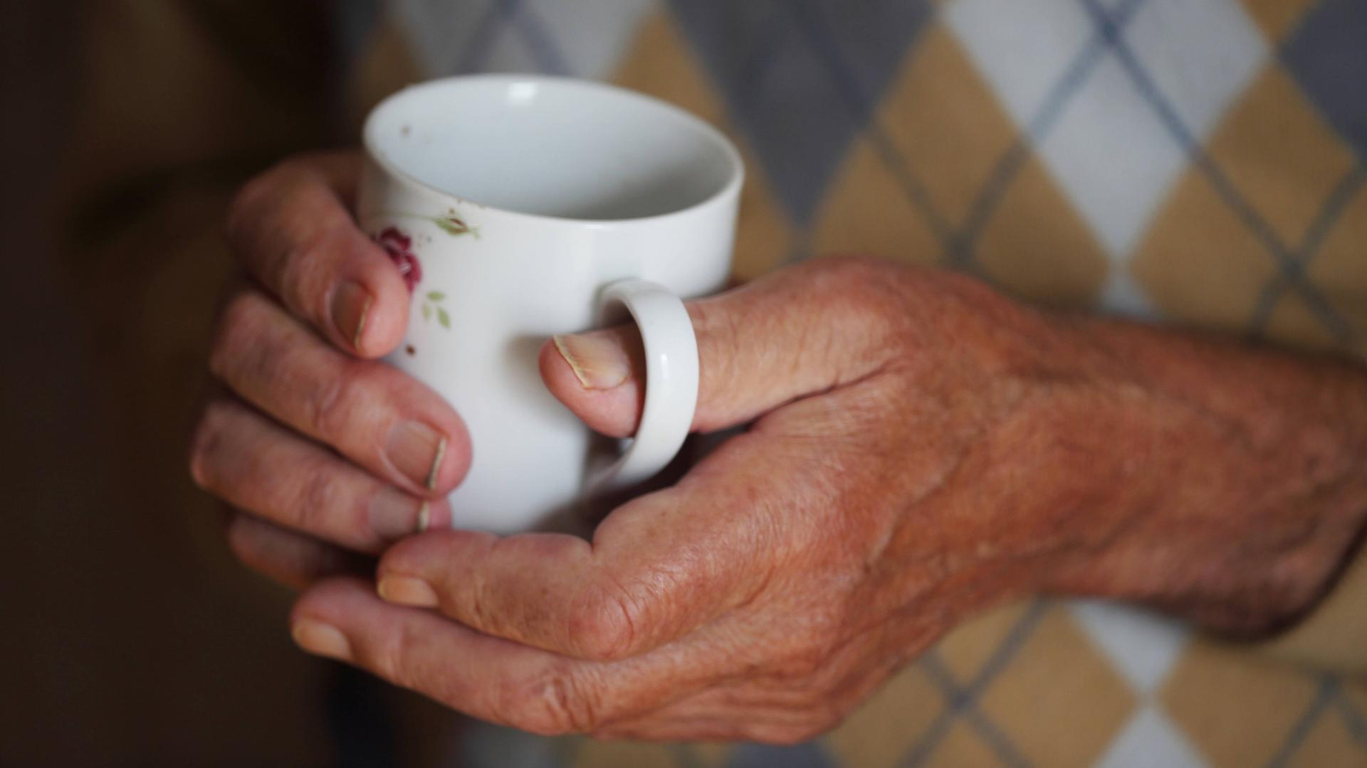 Ein älterer Mann hält eine wärmende Tasse Tee in den vom Alter gezeichneten Händen.
