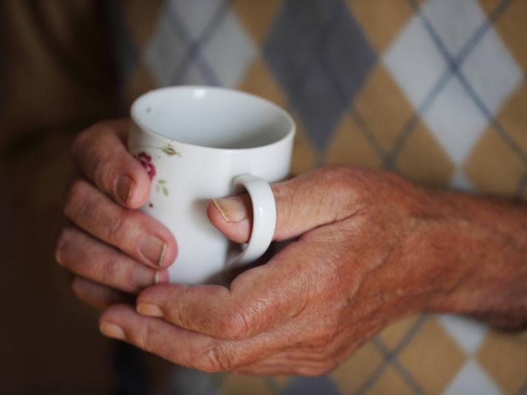 Ein älterer Mann hält eine wärmende Tasse Tee in den vom Alter gezeichneten Händen.