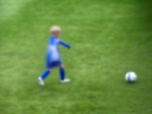 Ein Junge läuft mit einem Ball über einen Fußballplatz - er ist aber sehr unscharf fotografiert und damit nicht erkennbar.