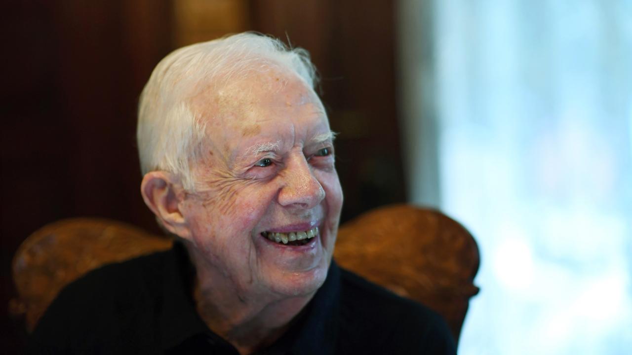 Der frühere Präsident der Vereinigten Staaten, Jimmy Carter, ist auf dem Bild Mitte 90. Er sitzt auf einem Sessel, schaut zur Seite und lacht.