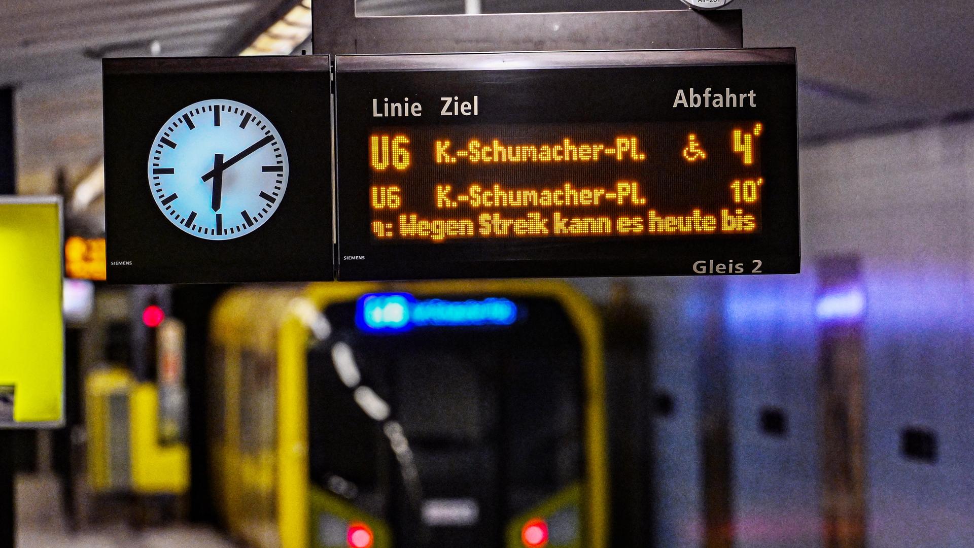 Ein Hinweisschild an einem Bahnsteig in Berlin der Linie U6, dass es wegen Streik zu Ausfällen kommen kann. Es ist 06.10 Uhr. Auf dem Gleis sieht man verschwommen einen Zug einfahren. 