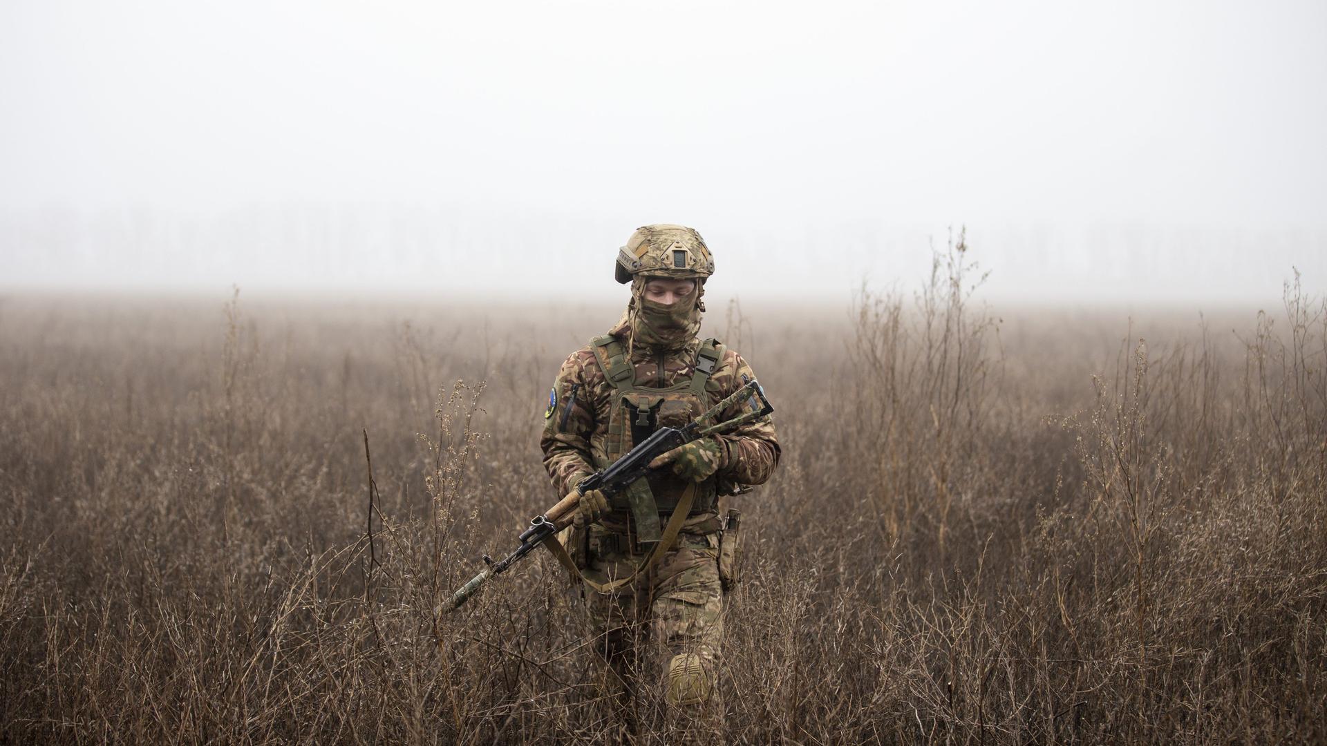 Ein ukrainischer Soldat läuft mit einer Waffe in der Hand über ein nebliges Feld.