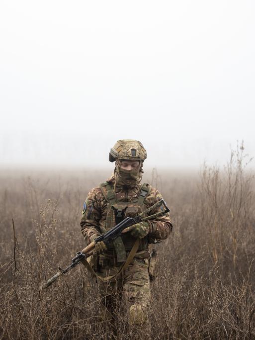 Ein ukrainischer Soldat läuft mit einer Waffe in der Hand über ein nebliges Feld.