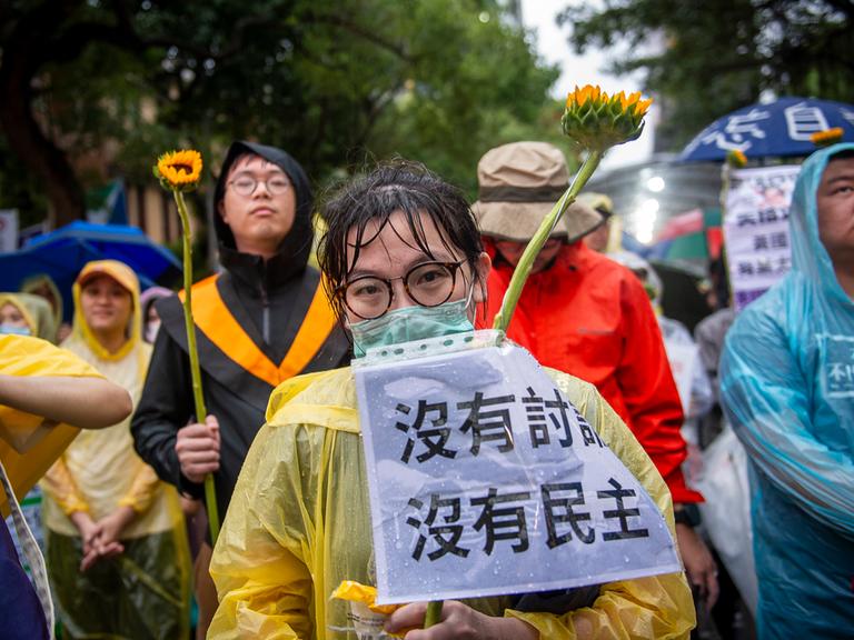 Demonstranten versammeln sich im Regen vor dem Yuan-Gebäude der Legislative in Taipeh, Taiwan, um gegen umstrittene Gesetzesentwürfe zu protestieren, sie halten Sonnenblumen in den Händen, 2024.