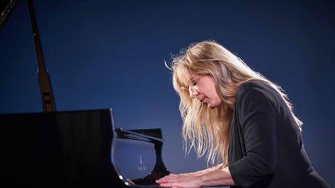 Ragna Schirmer spielt an einem Flügel, während ihr ihr langes, blondes Haar wild ins Gesicht fällt.