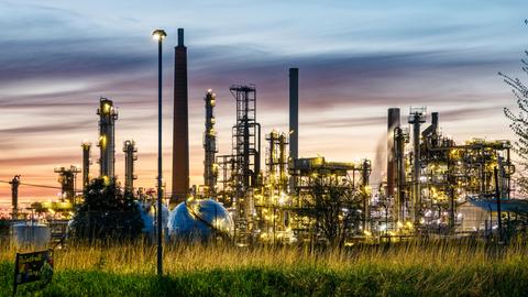 Die Raffinerie Heide GmbH mit beleuchteten Türmen und Industrieanlagen im Abendlicht.