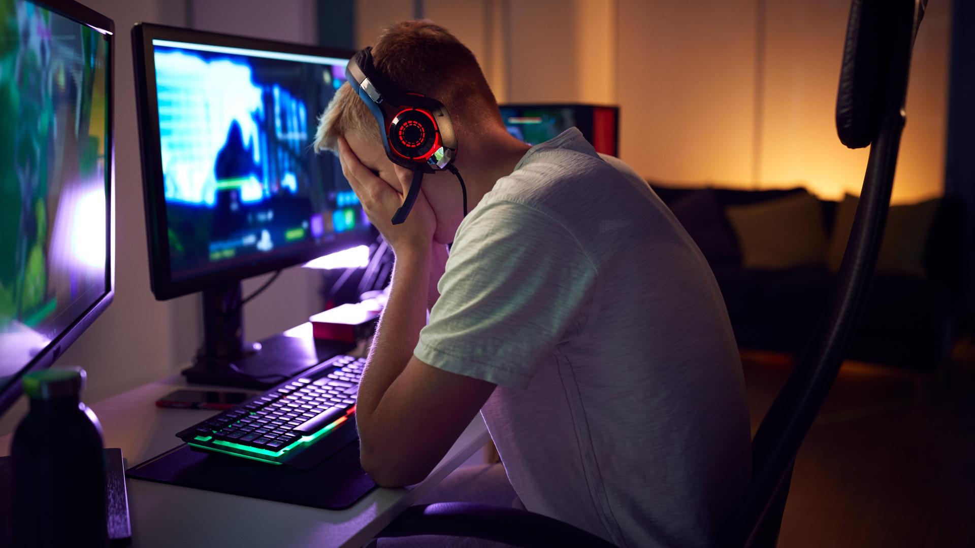 Ein Jugendlicher sitzt vor seinem Computer. Er hat Kopfhörer auf und die Hände vor das Gesicht gelegt. Ein Jugendlicher sitzt vor seinem Computer. Er hat Kopfhörer auf und die Hände vor das Gesicht gelegt.