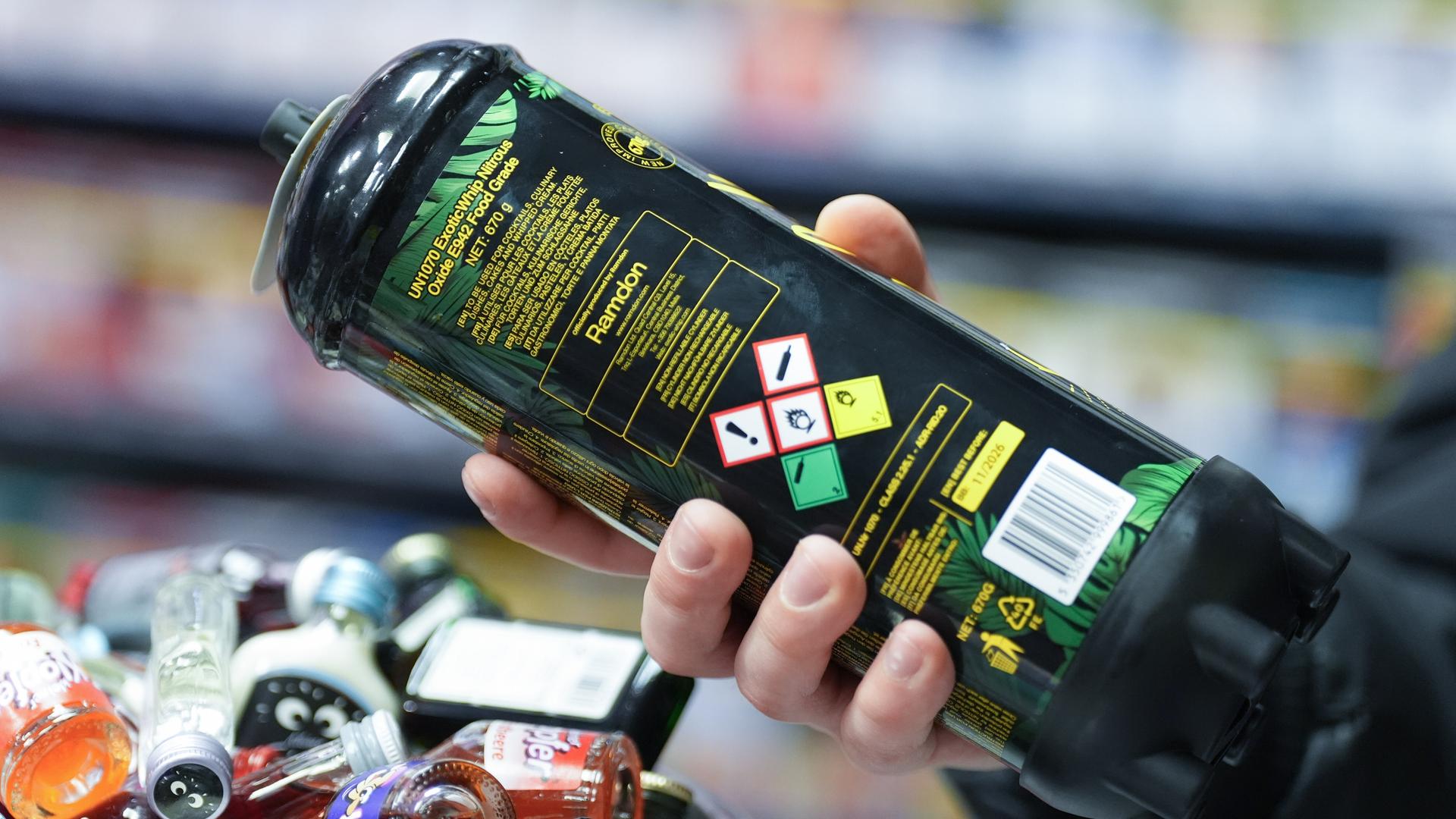 Ein Mitarbeiter hält eine Dose Lachgas am Tresen eines Kiosks in der Hand. Ein Mitarbeiter hält eine Dose Lachgas am Tresen eines Kiosks in der Hand.