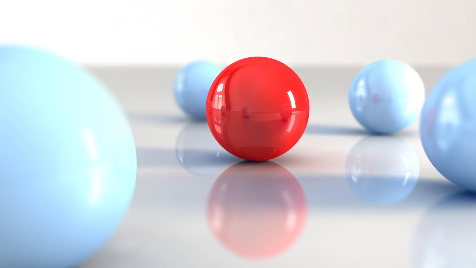 Eine rote Kugel ist von blauen umgeben auf einer spiegelglatten Unterlage. 