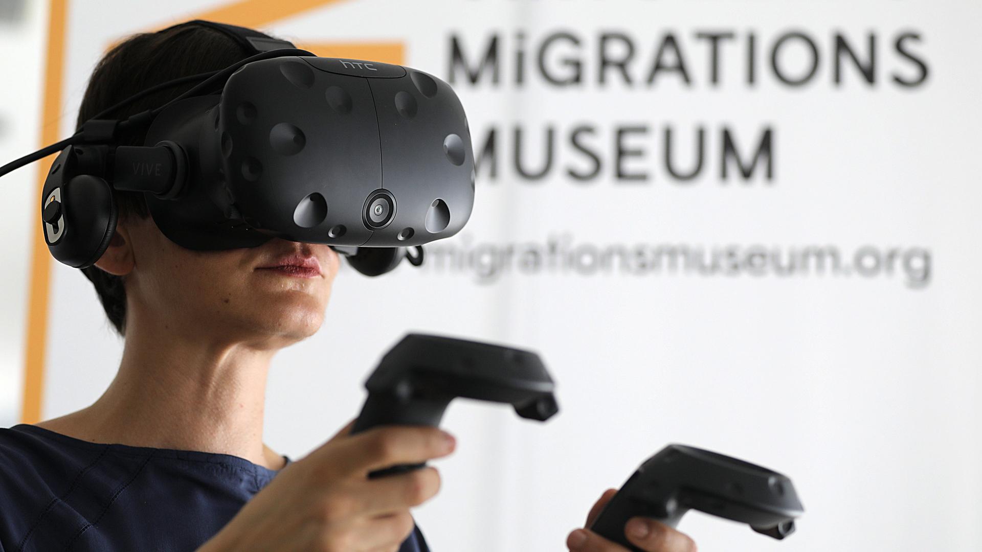 Eine Mitarbeiterin steht mit einer VR-Brille im Virtuellen Migrationsmuseum in Köln. Besucher des Museums können sich anhand digitaler Straßenszenen, Gebäuden und Objekten mit der Migrationsgeschichte auseinandersetzten. Dafür werden Virtual-Reality-Brillen (VR) genutzt. 