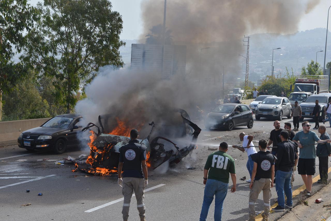 Libanon, Jiyeh: Sicherheitskräfte und Rettungskräfte versammeln sich um ein brennendes Fahrzeug am Schauplatz eines israelischen Luftangriffs, bei dem ein Auto getroffen wurde. 