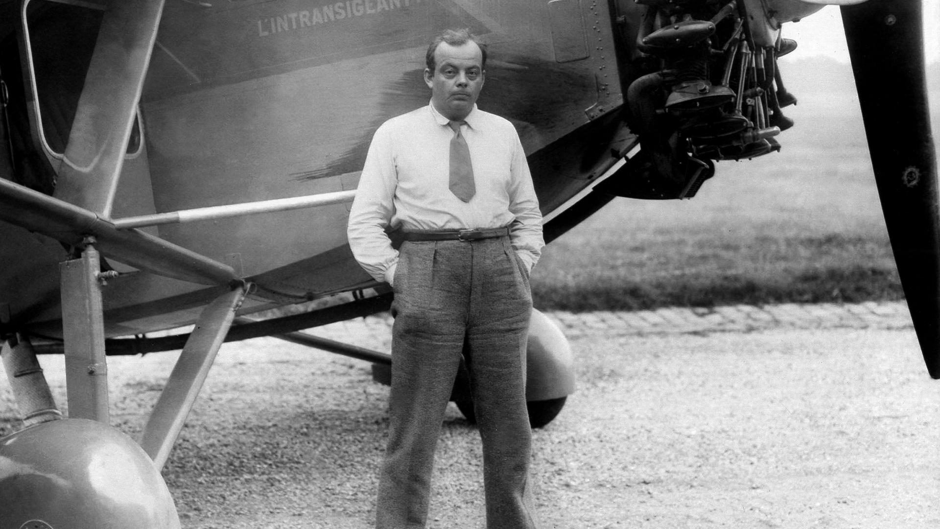 Schwarzßweiss Foto von Schriftsteller und Flieger Antoine de Saint-Exupery der vor einem Flugzeug steht.