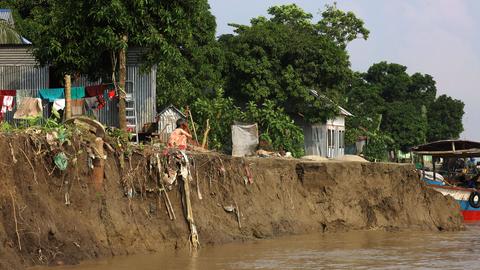 Ein Mann hockt vor seinem Haus am Padma-Fluss in Lauhjong, Bangladesch. Das Erdreich ist abgerutscht, die Wurzeln der Bäume sind sichtbar und das Wasser steht gefährlich nah an den Häusern, 10. Oktober 2023.