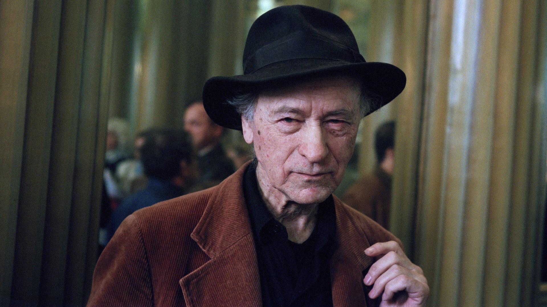Ein Porträt Jonas Mekas'. Er trägt einen schwarzen Hut und eine braune Jacke.