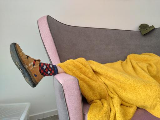 Eine Person liegt zugedeckt auf einem Sofa. Unter der Decke schaut ein Fuß heraus, der in einem Hausschuh und bunt gemusterten Socken steckt.