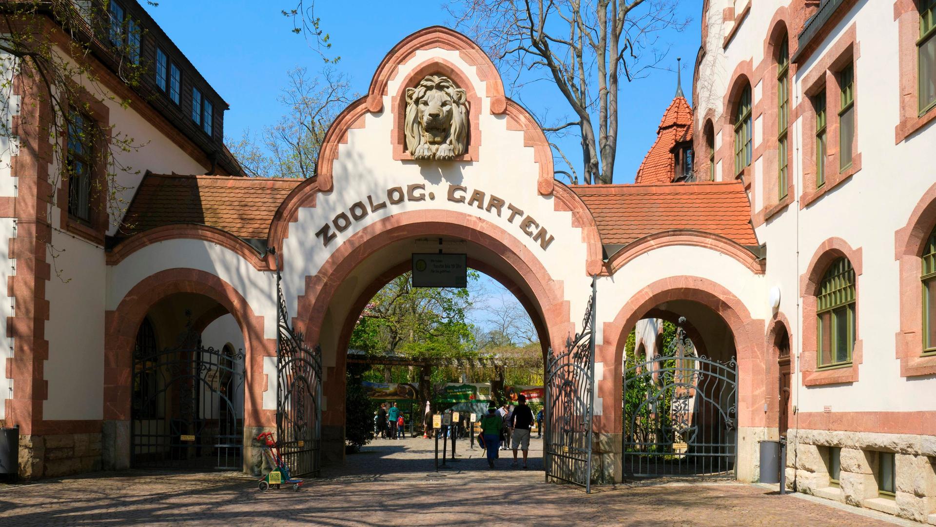 Eingang des Leipziger Zoos. Ein backsteingedecktes Tor mit drei Bögen. Den mittleren Bogen ziert ein Löwenkopf und die Aufschrift "Zoolog. Garten".
