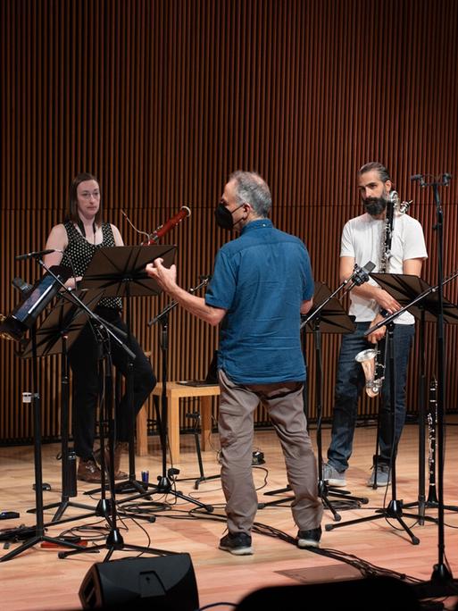 Die 5 Musiker des Ensembles stehen mit ihren Instrumenten auf der Bühne während der Komponist ihnen etwas erklärt