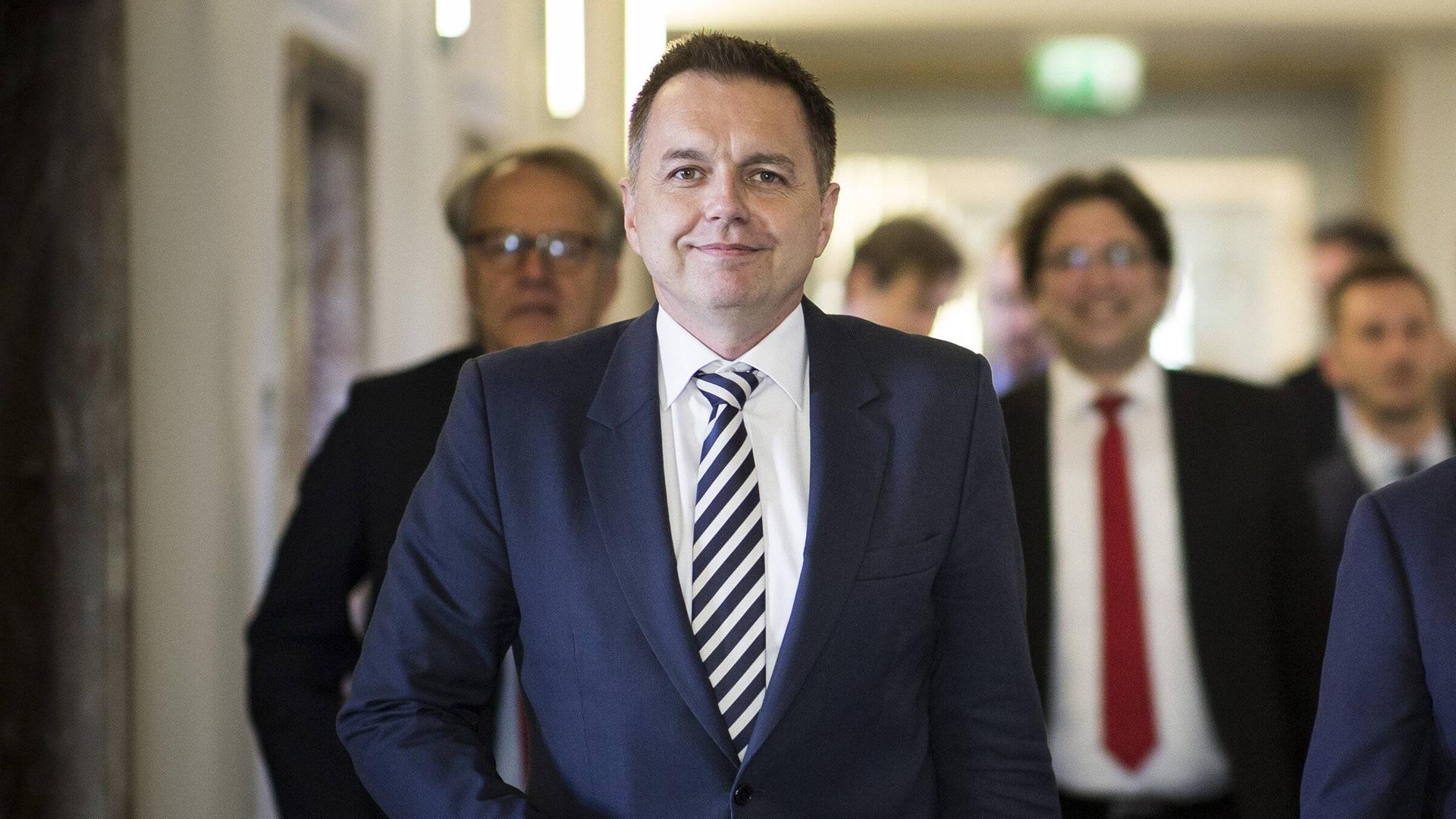 Das Foto zeigt einen Mann im blauen Anzug, der mit angewinkeltem, rechten Arm auf die Kamera zuläuft.