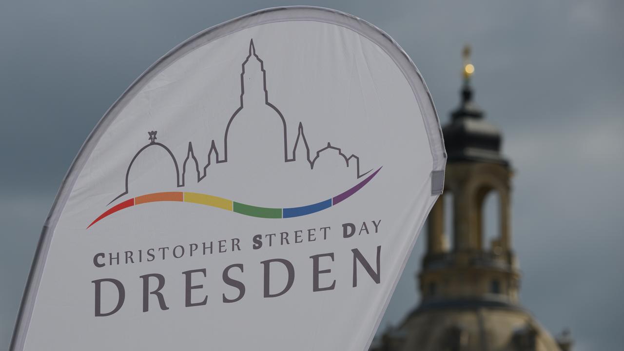 Eine Fahne mit dem Logo und der Aufschrift "Christopher Street Day Dresden" weht auf dem Altmarkt der sächsischen Stadt im Wind.